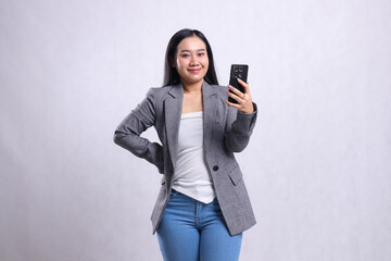 Naklejka premium beautiful young office woman asia smile to camera hold waist, holding cellphone wearing grey suit isolated on white background. for technology, lifestyle, shopping, transaction content