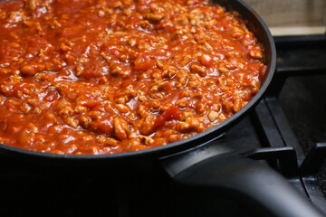 Spaghetti in a frying pan on a gas stove. Preparing lunch in a home kitchen. Fresh pasta and sauce cooking. Ready meal. Culinary background. Dinner preparation, homemade food.