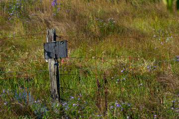 An image of an old rotten fence post with a faded and falling apart no trespassing sign. 