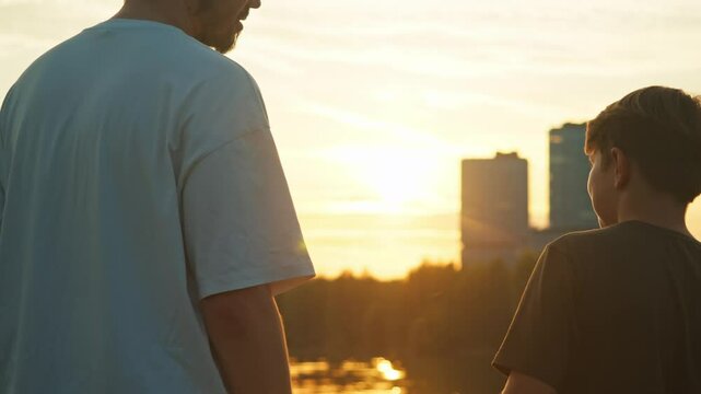 The older sibling embraces the younger sibling against the backdrop of a picturesque sunset in a metropolitan setting.