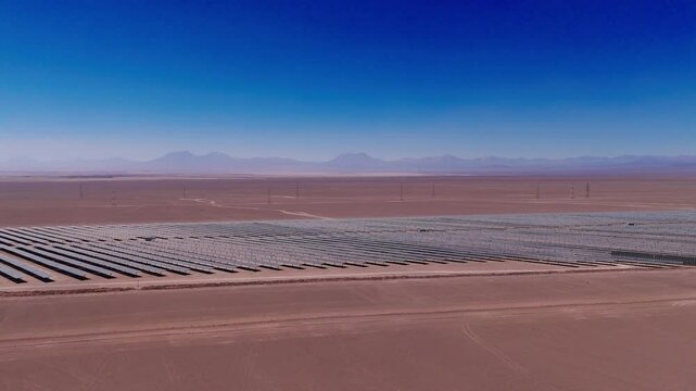 drone captura uma vista a&eacute;rea de um parque solar no deserto, exibindo c&eacute;lulas fotovoltaicas e m&oacute;dulos solares sob o c&eacute;u ensolarado