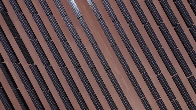 drone captura uma vista a&eacute;rea de um parque solar no deserto, exibindo c&eacute;lulas fotovoltaicas e m&oacute;dulos solares sob o c&eacute;u ensolarado