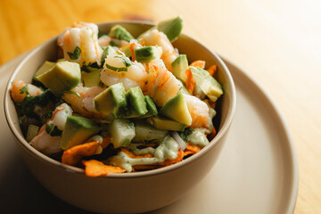 A bowl of shrimp, avocado, carrots, and other veggies on a plate