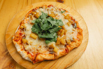 A pizza topped with pineapple and spinach on a wooden board