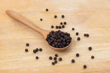 Whole black pepper on a wooden spoon. Peppercorn with a wooden spoon on a wooden cutting board background. The composition is isolated from the background.