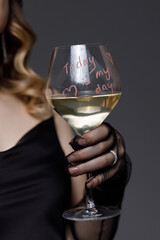 Woman holding a glass of white wine with a festive message at an evening celebration