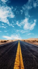 Naklejka premium A long, straight asphalt road stretches towards the horizon under a bright blue sky with fluffy white clouds.