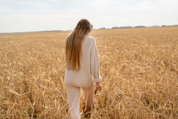 A woman walks through a vibrant wheat field under a sunny blue sky, enjoying natures beauty