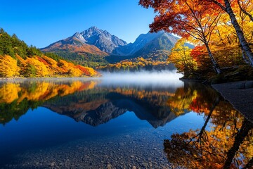 Fototapeta premium Mountain lake in autumn, reflecting the colorful trees and distant mountains, with a misty morning fog hanging low over the water