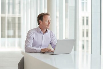 Fototapeta premium businessman working on computer in office man sits at an office desk, his laptop with the company in white and grey tones. He exudes confidence as he navigates through data