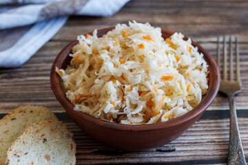 Homemade fermented cabbage with carrot Sauerkraut in bowl with fork and bread on wooden table background