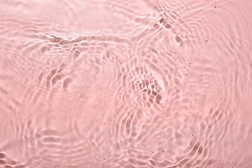 Rippled surface of clear water on pink background, top view