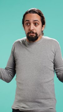 Vertical video Man shrugging shoulders, unable to provide answer, having detached apathy facial expression. Apathetic person doing hand gesturing showing lack of knowledge, studio background, camera B