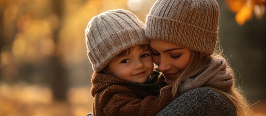 Obraz premium Close up of a mother and son cuddling in an autumn forest, both wearing knitted hats and sweaters.