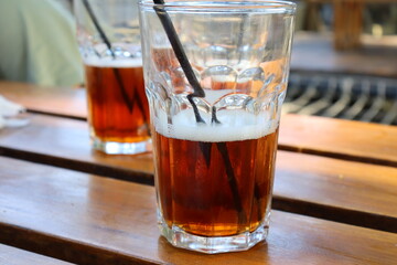 A glass of iced tea with a black straw and white foam on a wooden table. Concept of relaxation and enjoyment. 