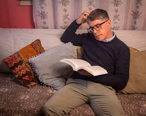 Fototapeta premium Adult man, sitting comfortably in an armchair reading a book