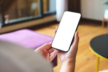 Mockup image of a woman holding mobile phone with blank desktop white screen at home