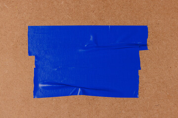 Blue adhesive sticky cloth tape is stick on brown wooden board surface to covering a portion of the surface.