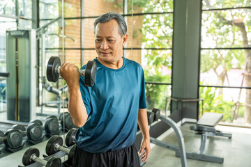Old man weight training wearing sportswear. Asian mature exercise indoor gym lifting dumbbell. Old...