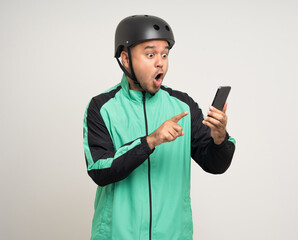 Young asian rider wearing green jacket uniform and bike helmet standing holding smartphone food application on isolated. Male delivery service worker. Delivery courier and shipping food service.