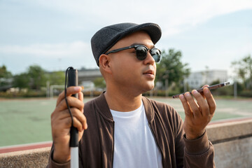 Young asian blind man using application on mobile phone to helping accessibility for persons with...