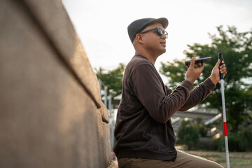 Young asian blind man using application on mobile phone to helping accessibility for persons with...