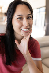 On video call, smiling woman in red shirt posing indoors, at home