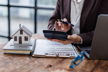Pressing calculators, hand plans home refinance. House model, buy or rent, calculators on desk....