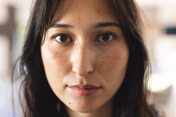Close-up of woman with freckles looking at camera with serious expression, at home