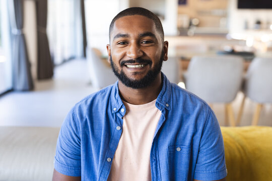 Smiling man in casual shirt sitting on couch during diverse friends hangout, at home