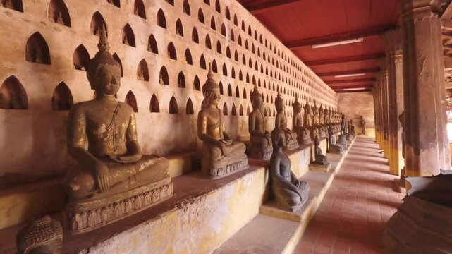Motion forward along the rows of many various old Buddha statues sitting in meditation Lotus pose in the courtyard of a Buddhist temple Wat Si Saket. Vientiane, Laos