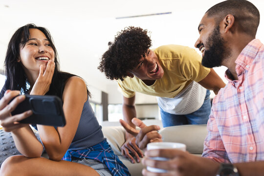 Diverse friends hanging out, laughing and enjoying time together with smartphone and coffee, at home