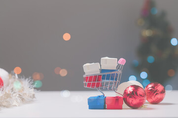 Miniature shopping cart filled with colorful gift boxes sits against softly blurred backdrop of holiday decorations, embodying joy of holiday shopping and festive preparations