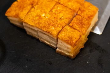 Crispy pork belly served on a black tray with spicy sauce