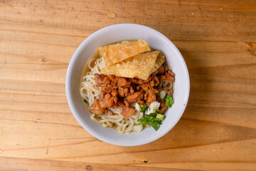 a bowl of chicken noodles, or mie ayam, on a wooden table
