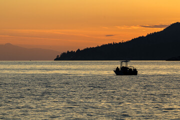 Fishermen on a boat near Bowen island at sunset, dusk or twilight with orange skies