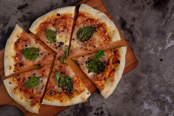 A slice of pizza with basil leaves on top. The pizza is cut into six pieces. The pizza is on a...