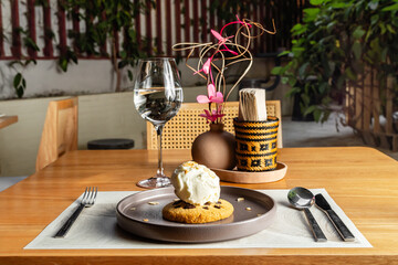 Tasty cookie with hazelnut chips and vanilla ice cream and nuts topping on a brown plate on a wooden table. Luxurious hotel restaurant.