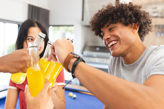 Diverse friends toasting with bottles of soda, enjoying time together indoors, at home