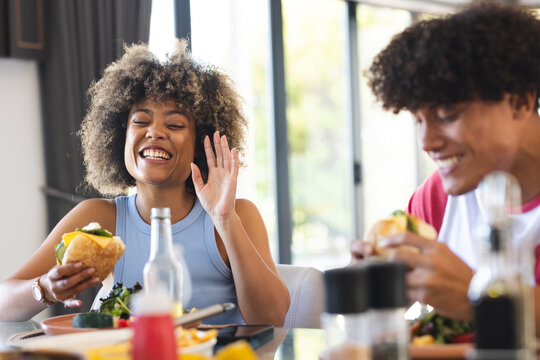 Eating burgers and laughing, diverse friends enjoying meal together at home - Powered by Adobe