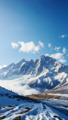 Fototapeta premium Vertical view of snow-covered mountain peaks with a clear blue sky and scattered clouds, highlighting the rugged terrain.
