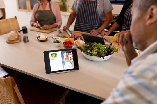 Following recipe on tablet, group of diverse friends preparing meal in kitchen, at home - Powered by Adobe