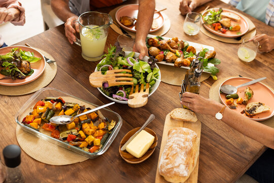 Sharing meal, diverse friends enjoying fresh salad, roasted vegetables, and bread together, at home