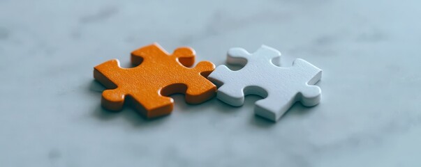 Fototapeta premium Two interlocking puzzle pieces, one orange and one white, placed on a smooth surface, symbolizing connection and problem-solving.