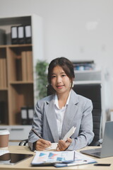 Successful Asian businesswoman smiling using laptop computer and holding coffee cup at office. Confident Asia businesswoman sitting happily in the office.