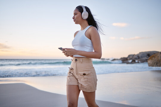 Beach, woman and thinking with smartphone on headphones for music, audio and radio in Brazil. Female person, seaside and satisfied on profile with streaming for motivational sound to relax on break - Powered by Adobe