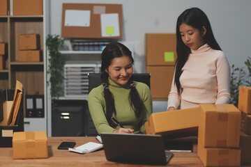 Startup SME small business entrepreneur of freelance Asian woman wearing apron using laptop and box to receive and review orders online to prepare to pack sell to customers, online sme business ideas.