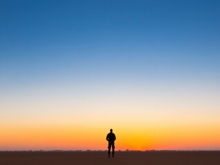 A solitary figure stands against a vibrant sunset, capturing the essence of tranquility and reflection in an expansive landscape.