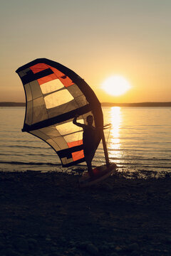 Man athlete comes out of the water with wing foil equipment at sunset.