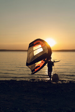 Man athlete comes out of the water with wing foil equipment at sunset.